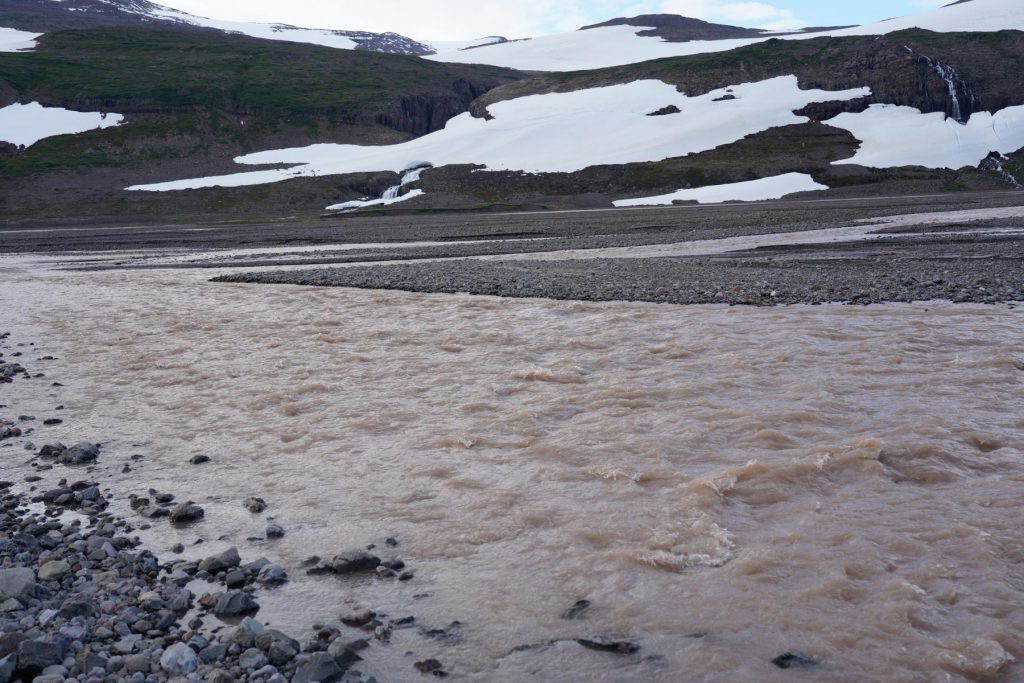 Stark strömender Flussarm mit Blick auf Schneefelder.